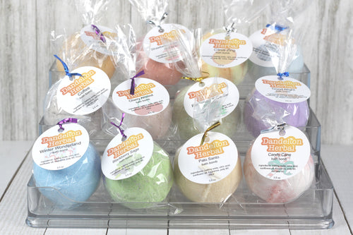 12 packaged bath bombs of various varieties on  a tiered clear plastic shelf.
